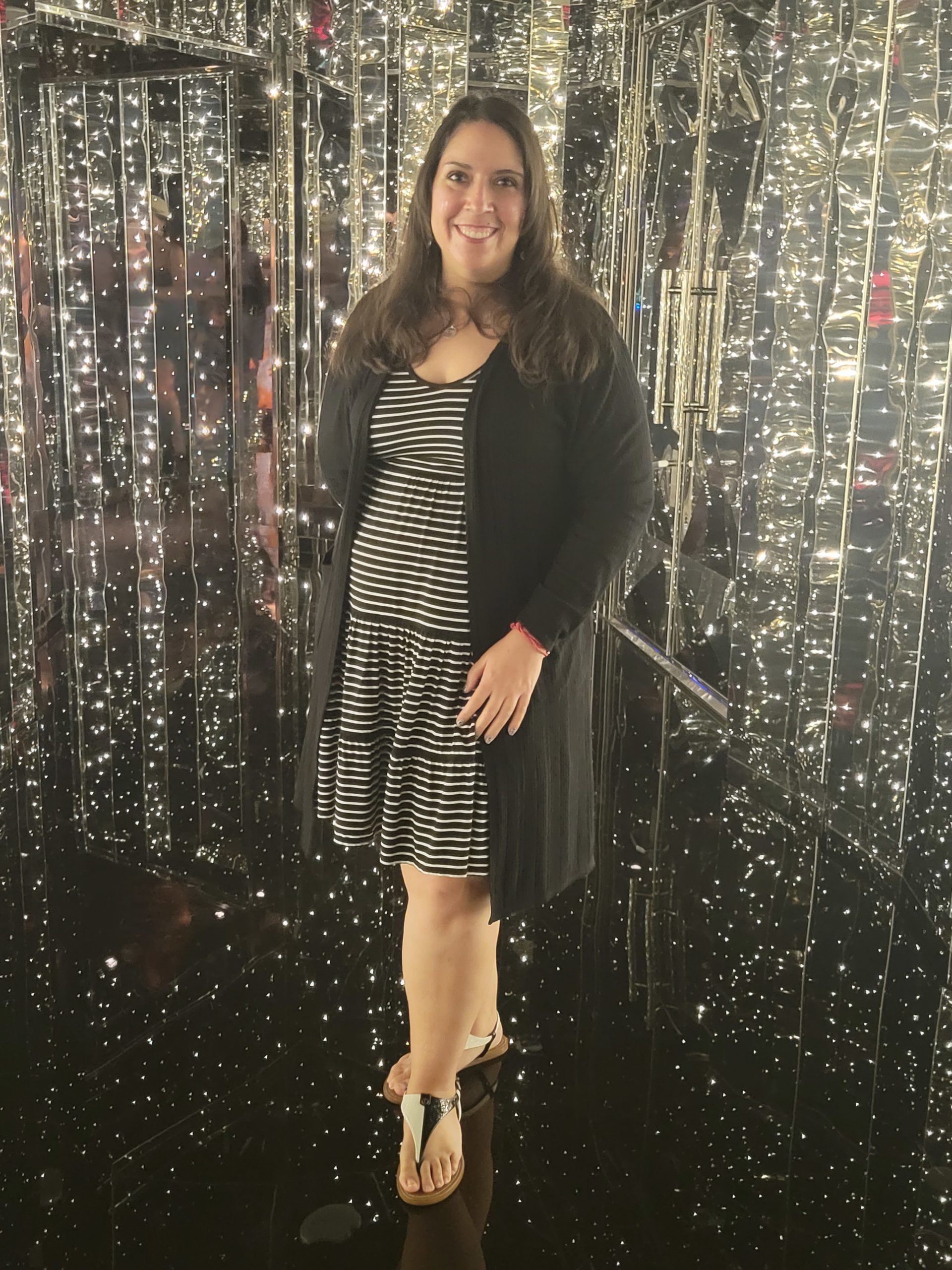 Millenial female standing in glittering hallway with black and white striped dress and black cardigan on.